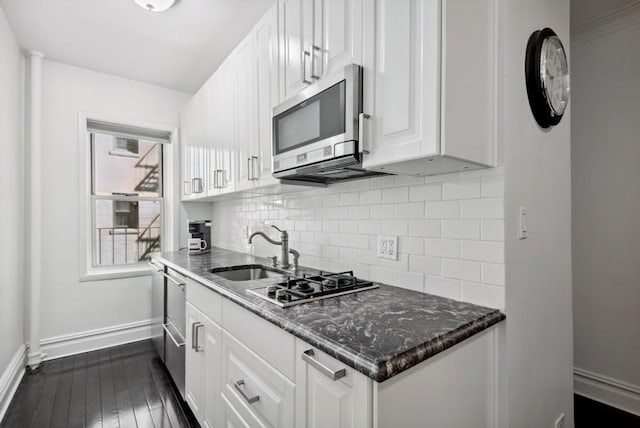 kitchen featuring stainless steel appliances, a sink, baseboards, tasteful backsplash, and white cabinetry