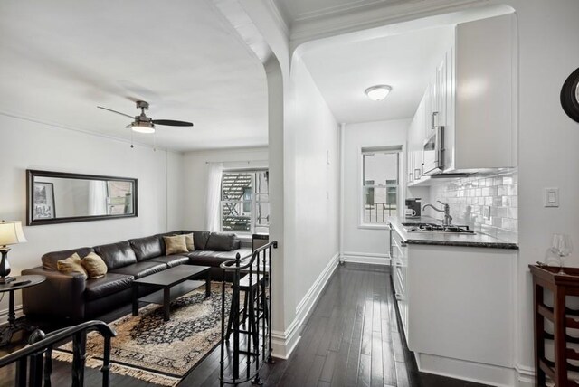 living area with ceiling fan, dark wood-style floors, baseboards, and arched walkways