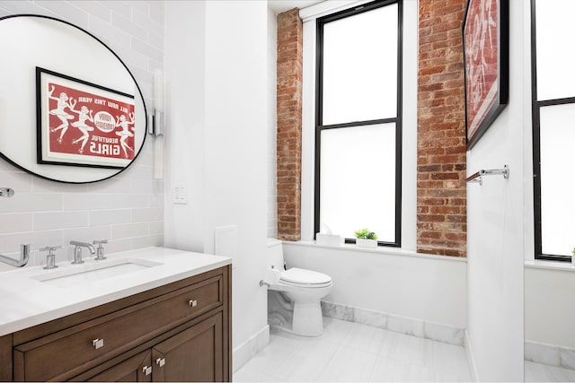 242 Lafayette St Unit 2N, New York City, NY 10012 - bathroom featuring healthy amount of natural light, baseboards, vanity, toilet, and brick wall