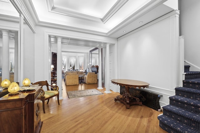 interior space with ornamental molding, stairs, a raised ceiling, decorative columns, and light wood finished floors