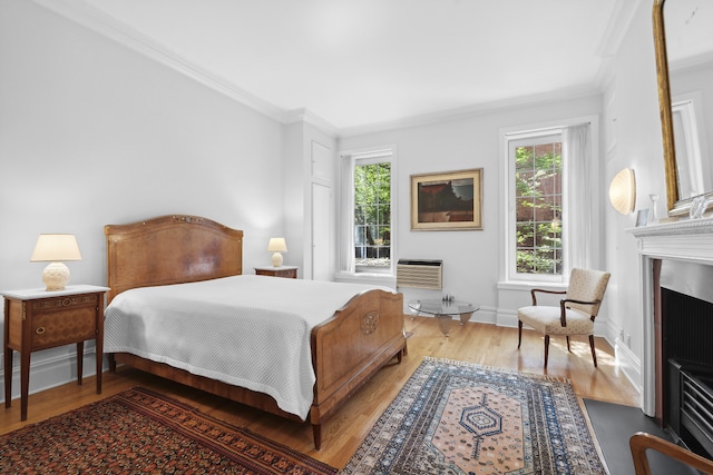 bedroom with a fireplace with flush hearth, crown molding, wood finished floors, and baseboards