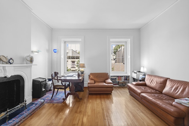 living area featuring light wood-type flooring, a healthy amount of sunlight, ornamental molding, and a fireplace with raised hearth