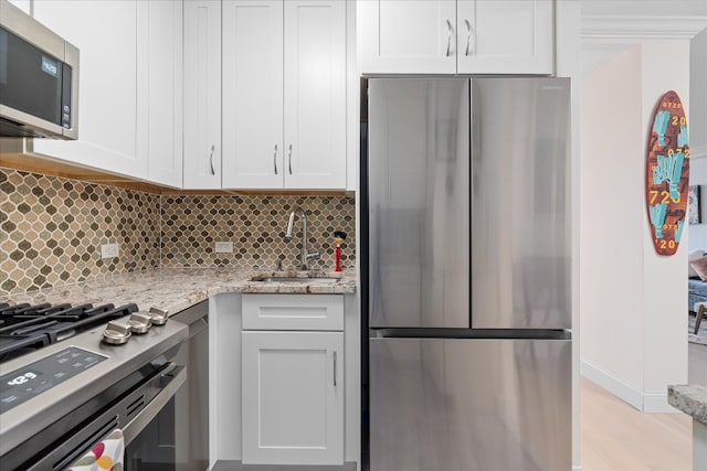 kitchen featuring white cabinets, light stone countertops, appliances with stainless steel finishes, a sink, and decorative backsplash
