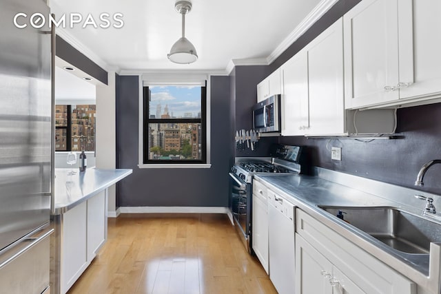 kitchen with appliances with stainless steel finishes, a sink, white cabinetry, ornamental molding, and light wood-style floors