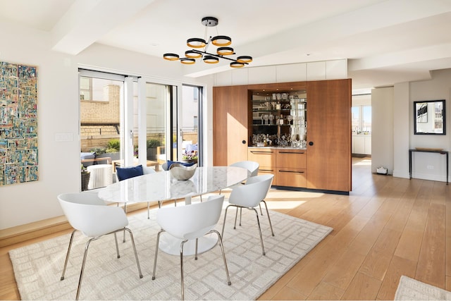 dining room featuring a bar, beam ceiling, a chandelier, and light wood-style flooring