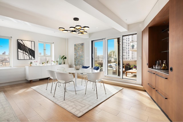 dining room with light wood-type flooring, an inviting chandelier, and beamed ceiling