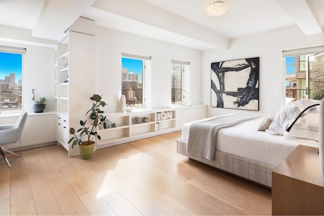 bedroom with light wood-type flooring, a city view, beam ceiling, and recessed lighting