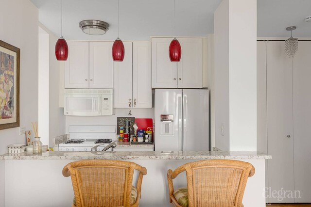 kitchen featuring white cabinets, hanging light fixtures, light stone counters, white appliances, and a peninsula