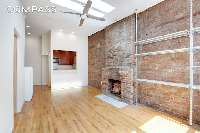 304 W 88th St Unit 4B, New York City, NY 10024 - unfurnished living room featuring a ceiling fan, wood finished floors, brick wall, a skylight, and a brick fireplace
