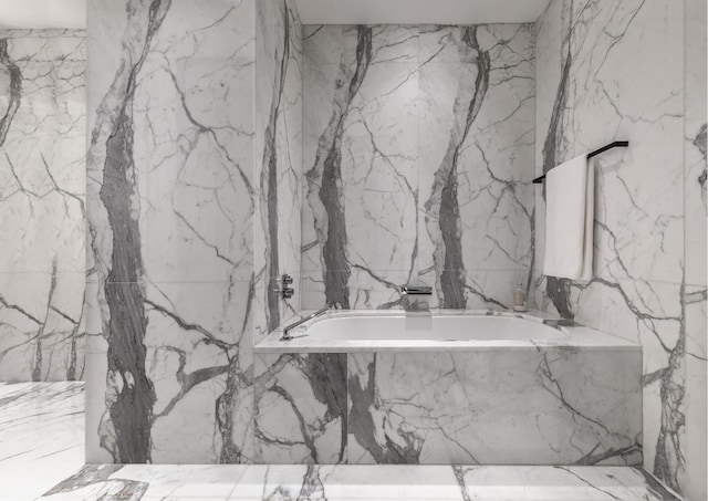 full bathroom with a tub with marble appearance and stone wall