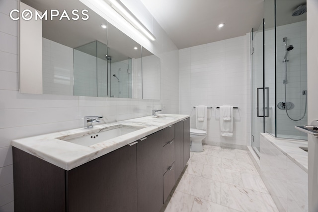 full bath featuring tile walls, a shower stall, double vanity, toilet, and marble look tile flooring