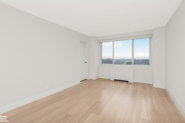 empty room featuring radiator, baseboards, and light wood-style flooring