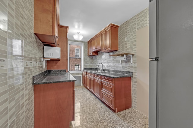kitchen featuring freestanding refrigerator, granite floors, a sink, white microwave, and dark stone counters