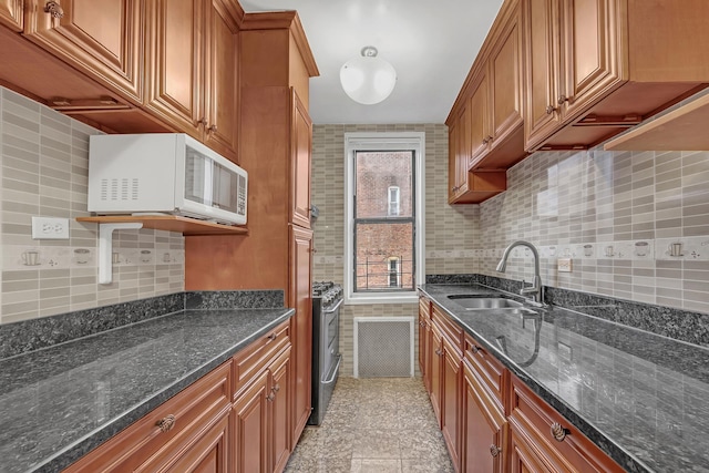 kitchen featuring white microwave, a sink, brown cabinets, tasteful backsplash, and dark stone counters
