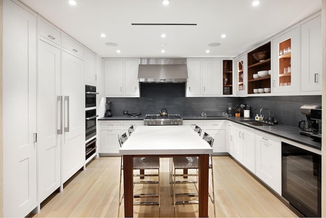 kitchen with white cabinets, a sink, wall chimney exhaust hood, wine cooler, and backsplash