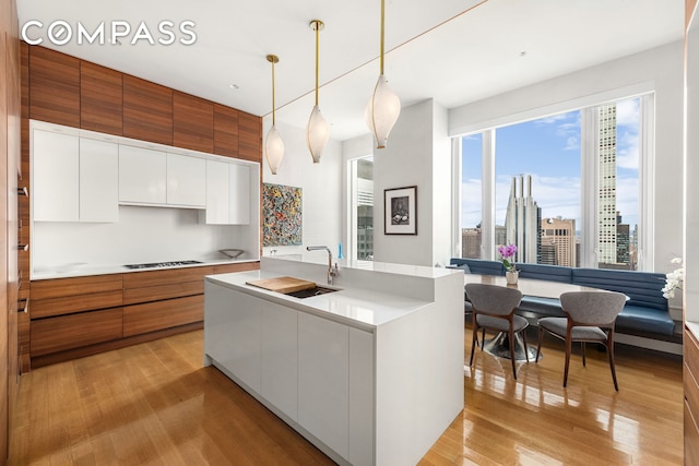 252 E 57th St Unit 60A, New York City, NY 10022 - kitchen featuring modern cabinets, brown cabinets, light wood-style flooring, black cooktop, and white cabinetry