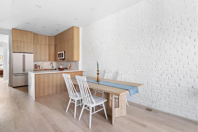 dining space featuring light wood-style floors and brick wall