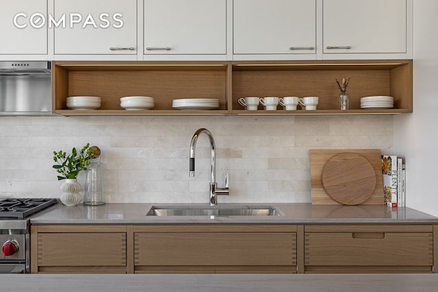 kitchen featuring open shelves, a sink, stainless steel range with gas cooktop, backsplash, and white cabinetry