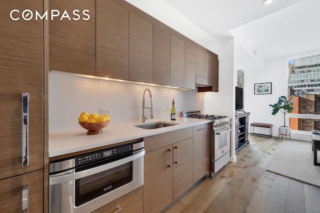 325 Lexington Ave Unit 16C, New York City, NY 10016 - kitchen featuring appliances with stainless steel finishes, a sink, light wood-style floors, modern cabinets, and light countertops