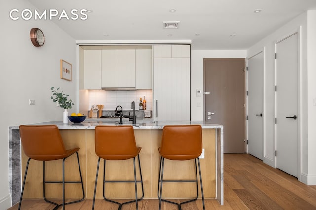 kitchen with light wood-style flooring, backsplash, a breakfast bar area, and a peninsula