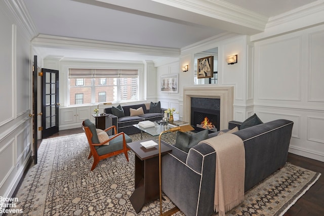living area with a lit fireplace, wood finished floors, ornamental molding, and a decorative wall