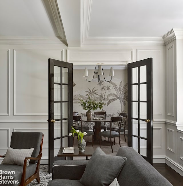 living area with dark wood-style floors, a notable chandelier, ornamental molding, and a decorative wall