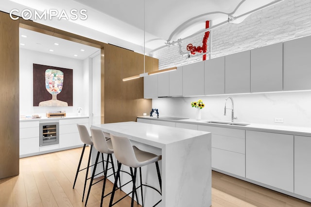 kitchen with modern cabinets, a sink, beverage cooler, light countertops, and light wood-type flooring