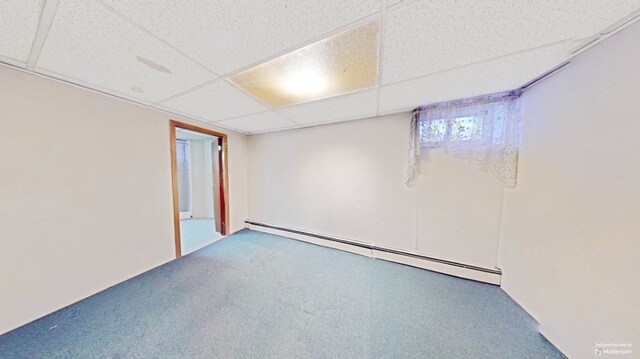 basement with a baseboard heating unit, carpet, and a paneled ceiling