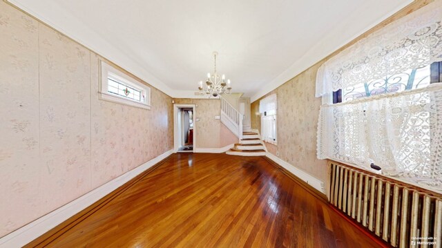 unfurnished dining area with wallpapered walls, baseboards, hardwood / wood-style flooring, stairs, and a notable chandelier