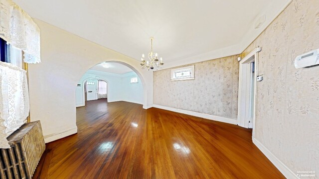 unfurnished dining area with arched walkways, radiator, baseboards, a chandelier, and hardwood / wood-style floors