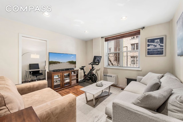 living area with radiator heating unit, wood finished floors, a wall unit AC, recessed lighting, and baseboards
