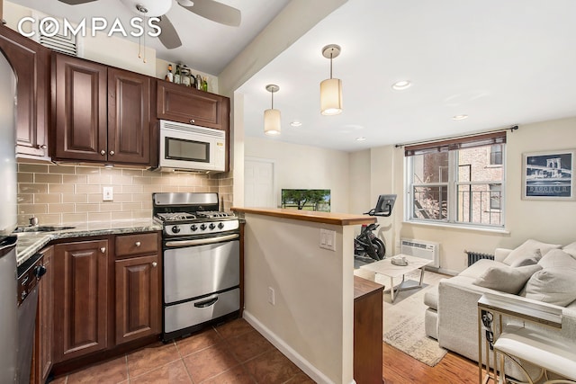 kitchen featuring white microwave, stainless steel gas stove, radiator heating unit, a peninsula, and backsplash