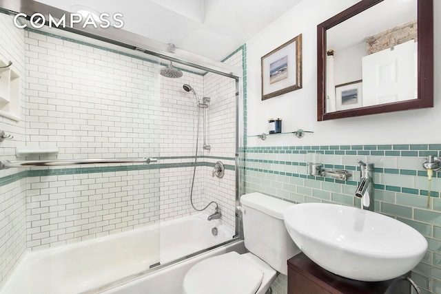 bathroom featuring a sink, enclosed tub / shower combo, tile walls, toilet, and wainscoting