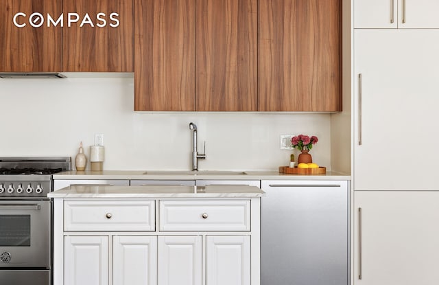 kitchen with high end appliances, light countertops, a sink, and white cabinets