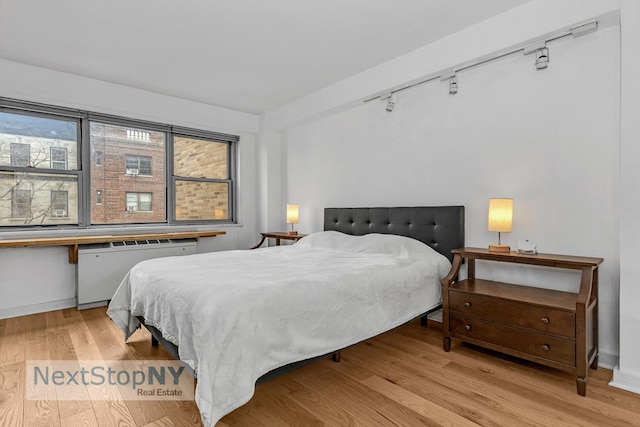 330 E 49th St Unit 6J, New York City, NY 10017 - bedroom with radiator heating unit, rail lighting, wood finished floors, and baseboards