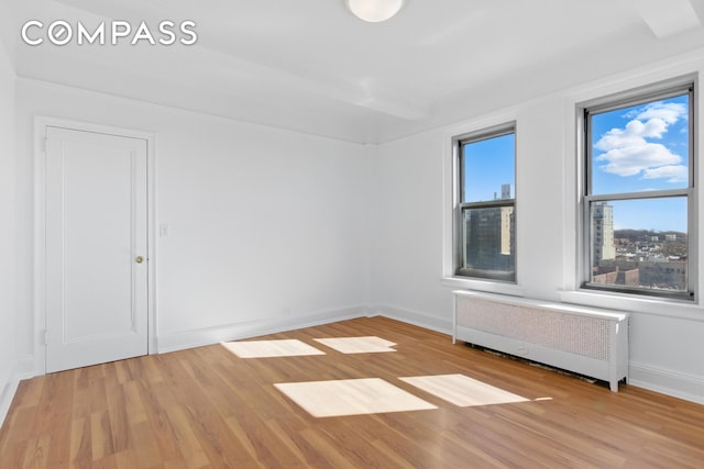 empty room with radiator heating unit, light wood-type flooring, and baseboards
