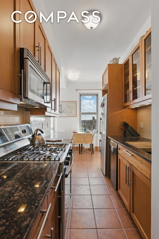 kitchen with appliances with stainless steel finishes, decorative backsplash, glass insert cabinets, and brown cabinetry