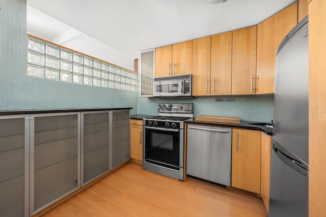 211 Thompson St Unit Lb, New York City, NY 10012 - kitchen featuring dark countertops, backsplash, stainless steel appliances, and light wood-type flooring