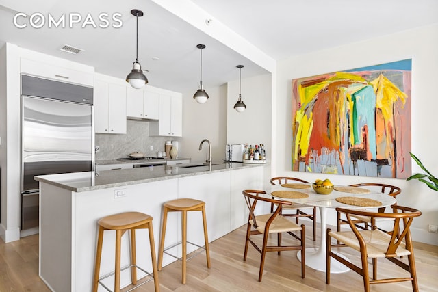kitchen featuring built in fridge, light wood finished floors, decorative backsplash, white cabinetry, and a sink