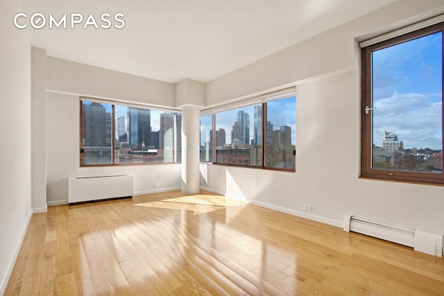 393 W 49th St Unit 6G, New York City, NY 10019 - spare room with radiator heating unit, a view of skyline, wood finished floors, and baseboards