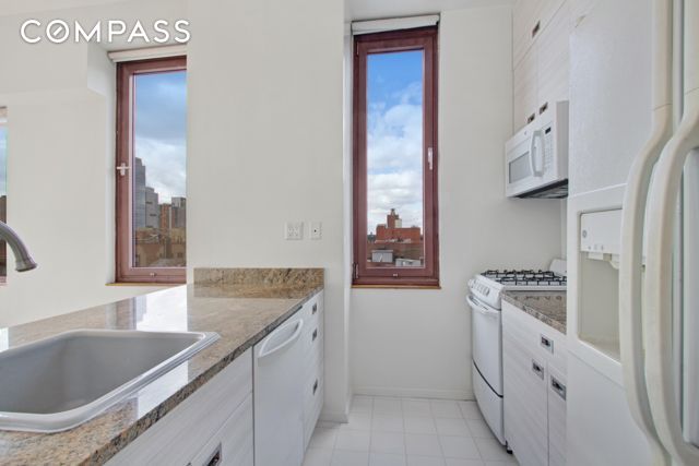 393 W 49th St Unit 6G, New York City, NY 10019 - kitchen with white appliances, a sink, white cabinetry, baseboards, and light stone counters