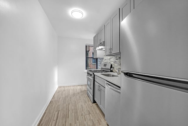 kitchen featuring decorative backsplash, appliances with stainless steel finishes, light wood finished floors, under cabinet range hood, and gray cabinetry