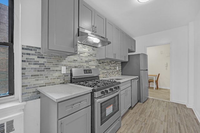 kitchen with light countertops, under cabinet range hood, stainless steel appliances, and gray cabinetry