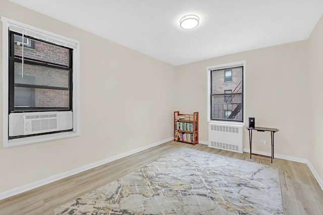 sitting room with radiator heating unit, baseboards, cooling unit, and wood finished floors
