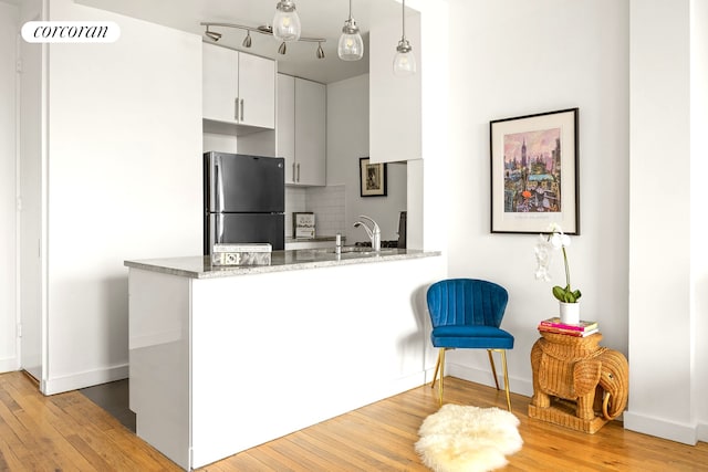 kitchen featuring a sink, freestanding refrigerator, light wood-type flooring, baseboards, and a peninsula