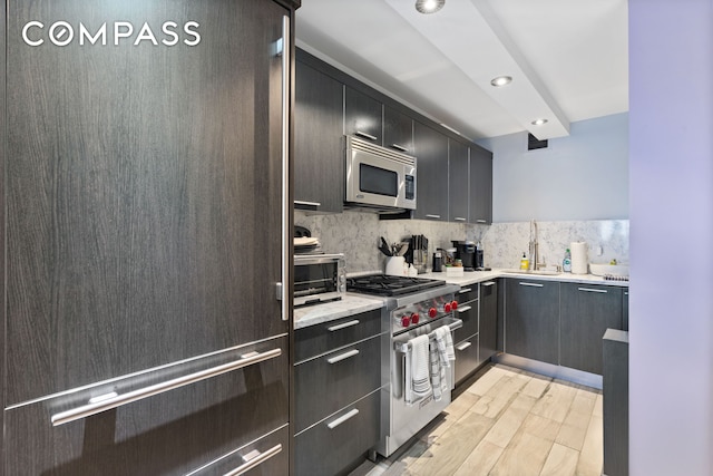 kitchen featuring premium appliances, a sink, light wood-style floors, tasteful backsplash, and recessed lighting