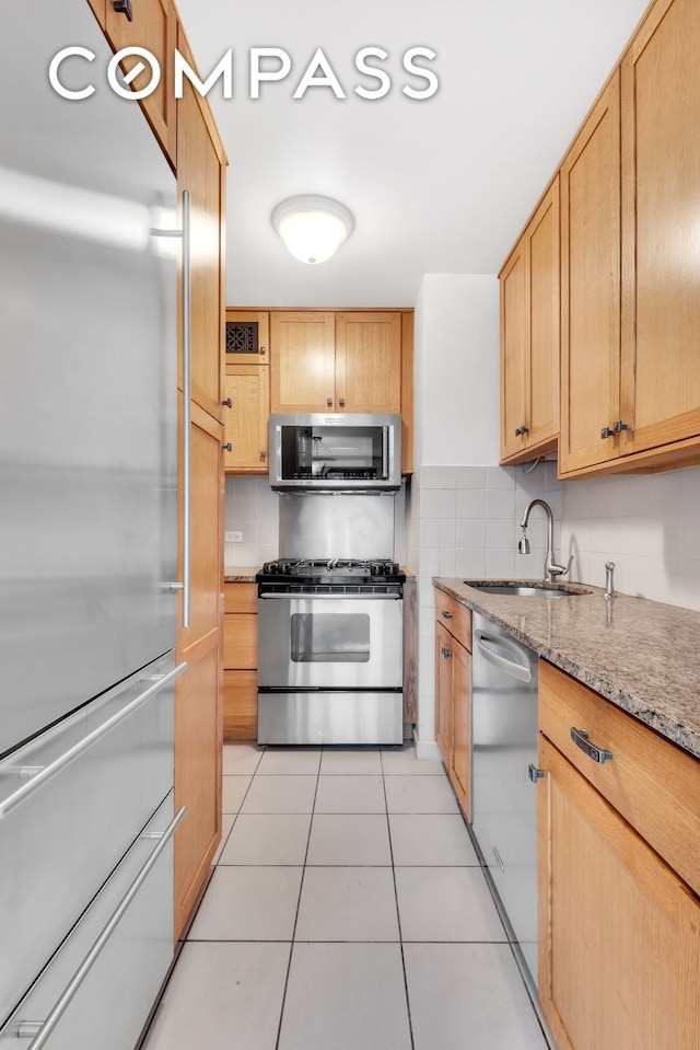 kitchen with light stone counters, a sink, stainless steel appliances, light tile patterned flooring, and backsplash