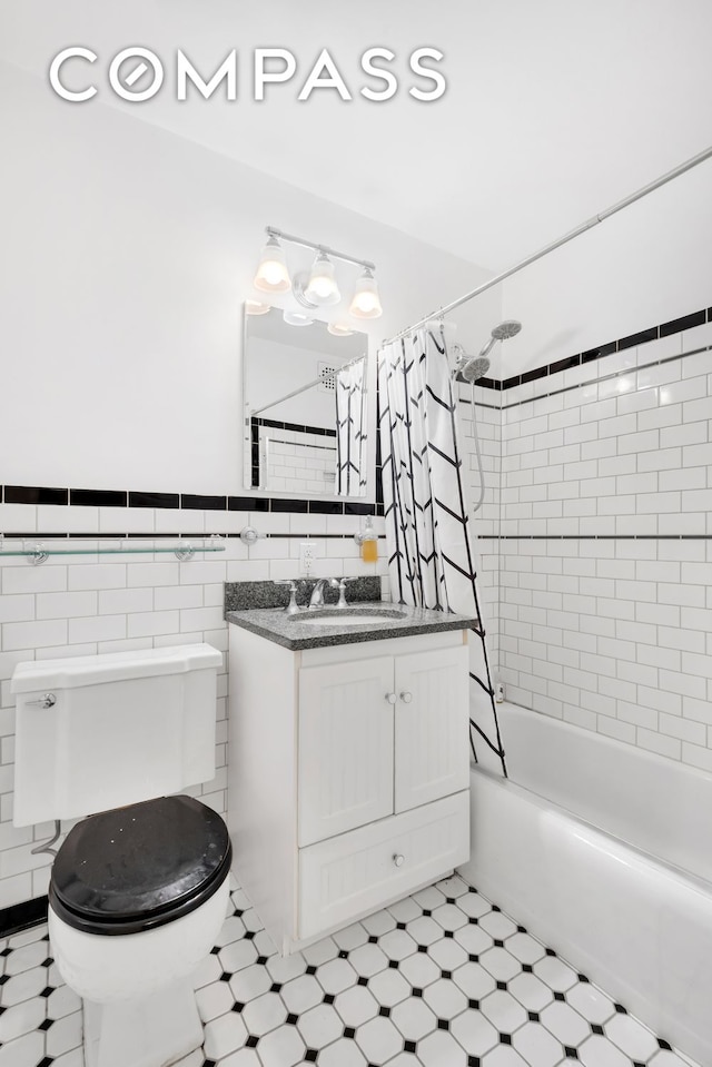 bathroom featuring tile walls, vanity, shower / bath combo with shower curtain, toilet, and wainscoting