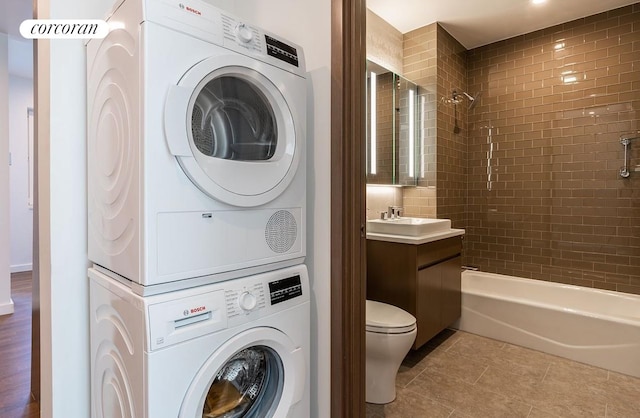 bathroom with stacked washer / drying machine, toilet, tile patterned flooring, washtub / shower combination, and vanity