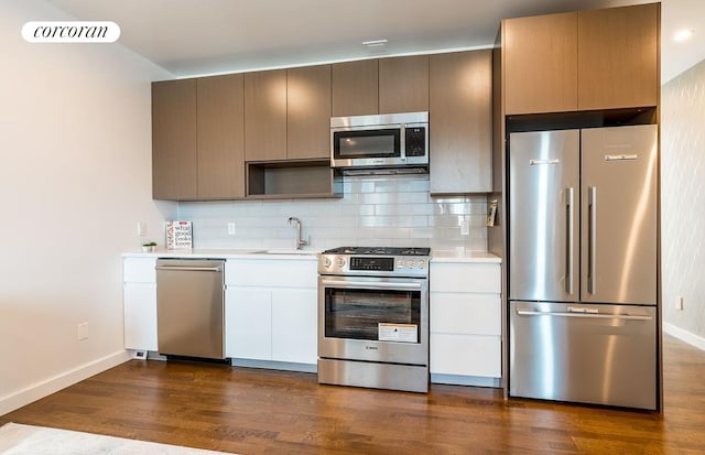 kitchen featuring appliances with stainless steel finishes, light countertops, a sink, baseboards, and tasteful backsplash